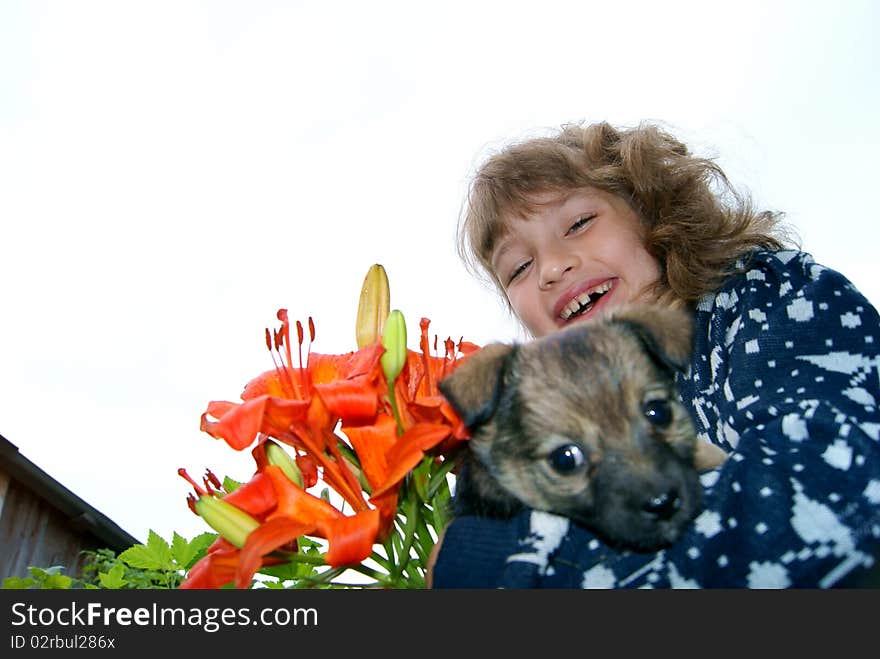 The joyful girl with flowers holds a small puppy on hands. The joyful girl with flowers holds a small puppy on hands