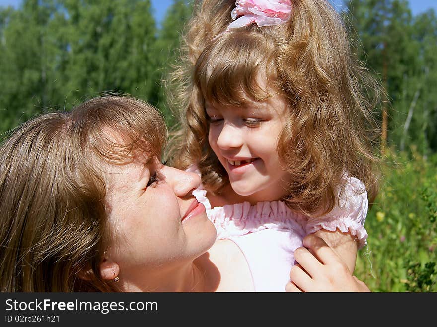 The laughing beautiful girl embraces the woman in the summer on the nature and looks at it. The laughing beautiful girl embraces the woman in the summer on the nature and looks at it