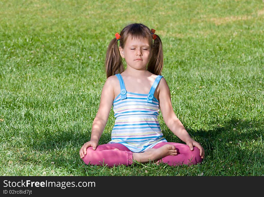 Little child sit and meditate in asana on grass