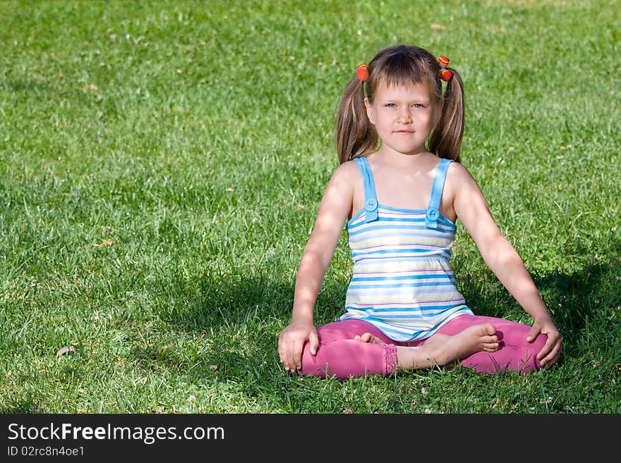 Little girl sits in the shade in asana on grass