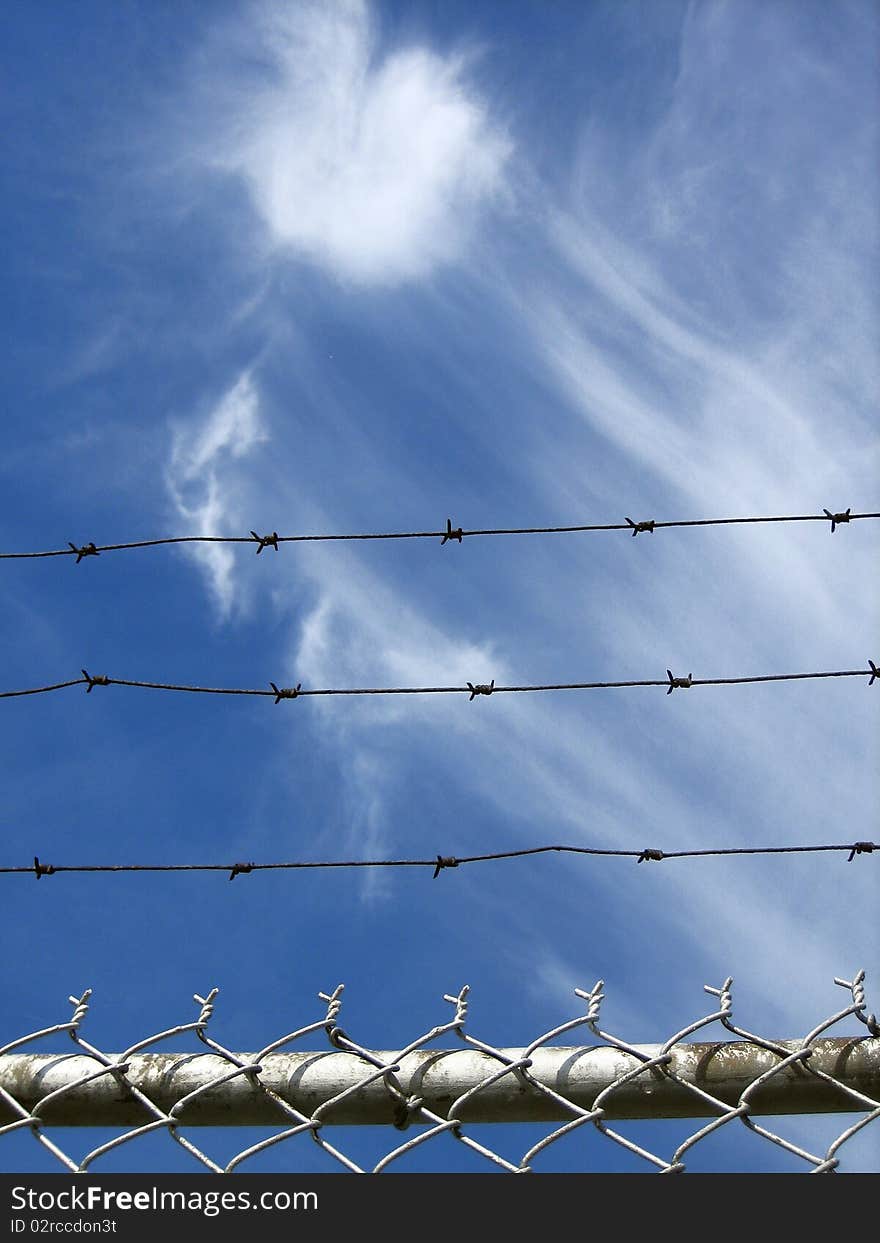 Dreamy, free-floating clouds in a beautiful blue sky behind a pointy barb wire fence. Dreamy, free-floating clouds in a beautiful blue sky behind a pointy barb wire fence.