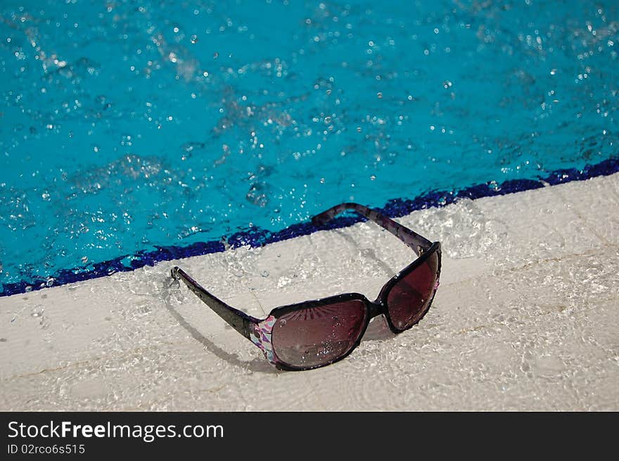 Splashed sunglasses lying by a swimming pool. Splashed sunglasses lying by a swimming pool