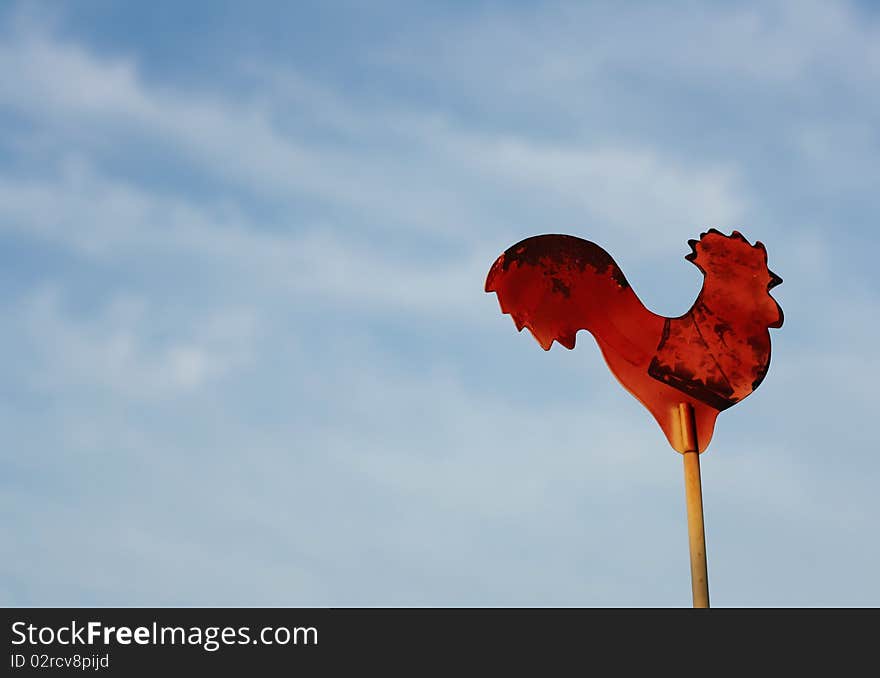 Vintage red rooster sign against a blue sky background with room for text.