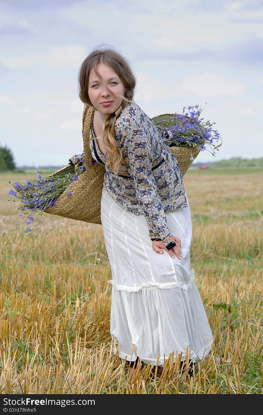 Woman in a white skirt closes eyes and holds a basket with flowers on a shoulder. Woman in a white skirt closes eyes and holds a basket with flowers on a shoulder