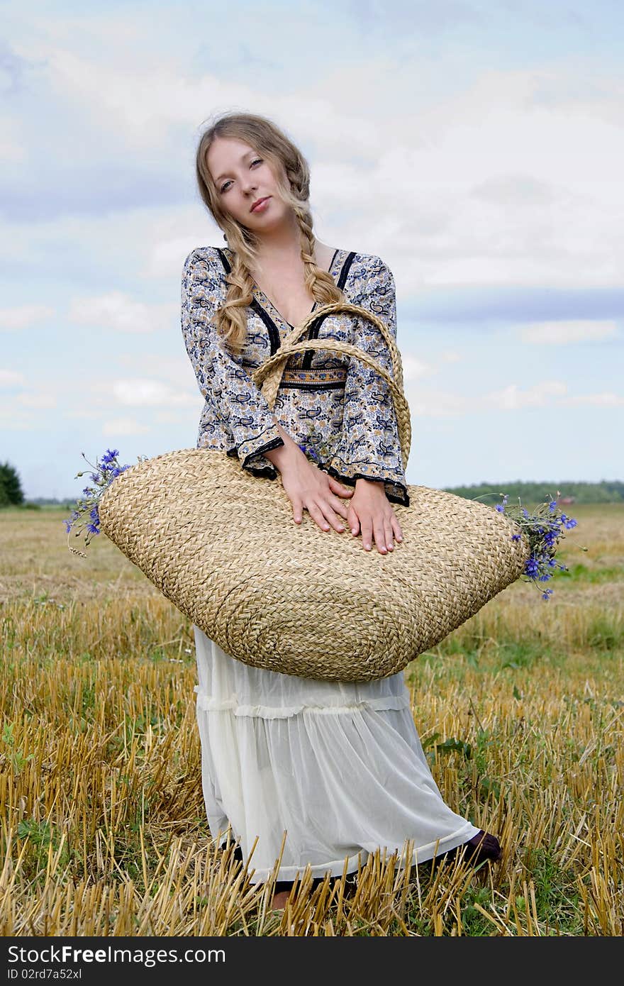 Woman in a white skirt closes eyes and holds a basket with flowers on a shoulder. Woman in a white skirt closes eyes and holds a basket with flowers on a shoulder