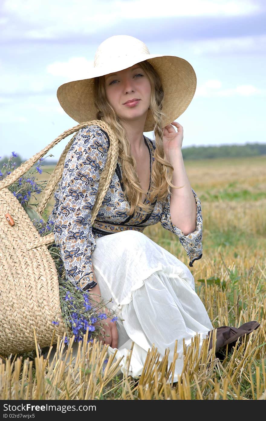 Woman in a hat sits in the summer in the field of with a basket of cornflowers. Woman in a hat sits in the summer in the field of with a basket of cornflowers