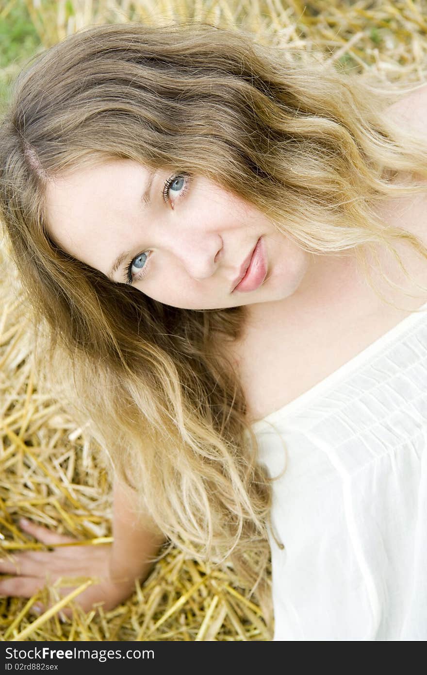 Woman with long hair and blue eyes sits and looks upwards in the summer on straw. Woman with long hair and blue eyes sits and looks upwards in the summer on straw