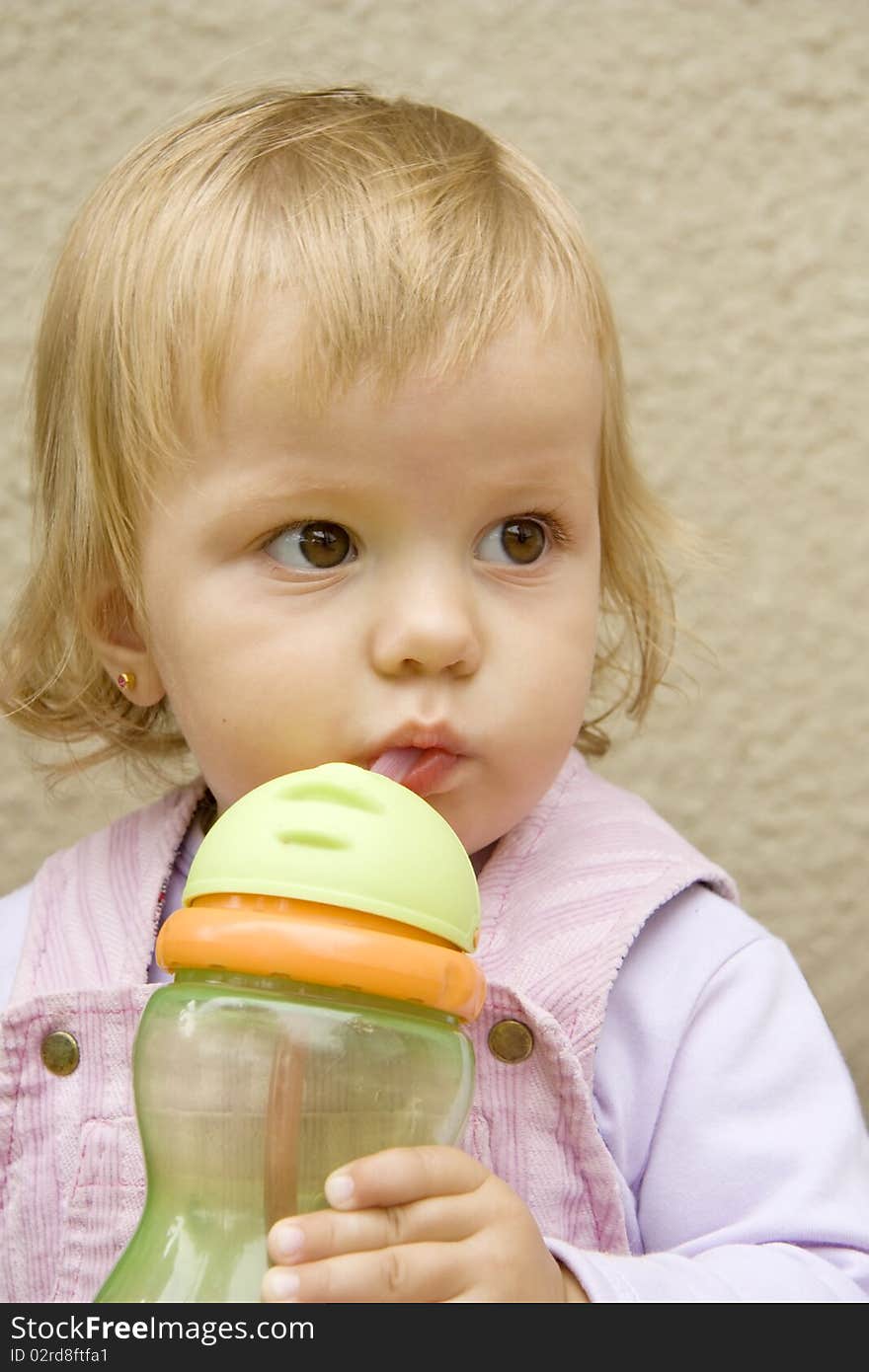 Little girl drinks from a small bottle and with interest looks aside. Little girl drinks from a small bottle and with interest looks aside