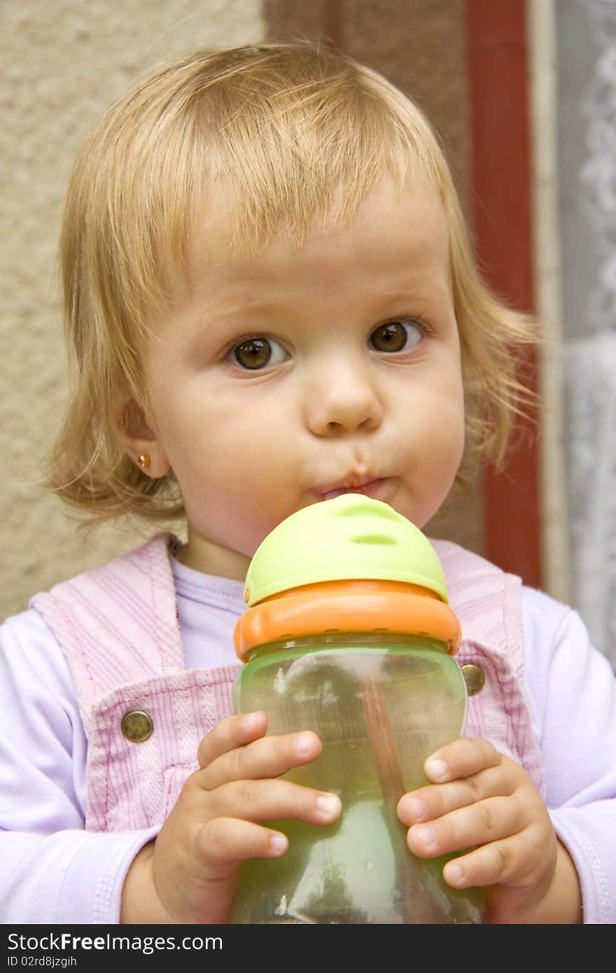 Little girl drinks from a small bottle and with interest looks aside. Little girl drinks from a small bottle and with interest looks aside