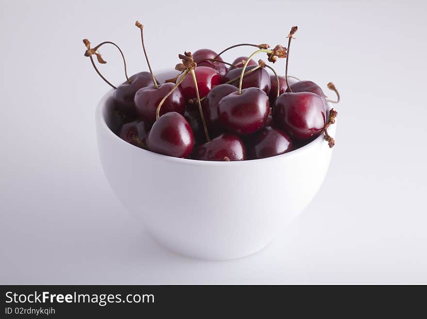 A white bowl of cherries on a white background.