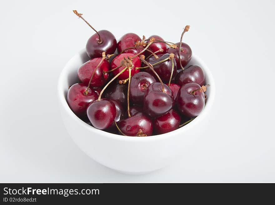 A white bowl of cherries on a white background.