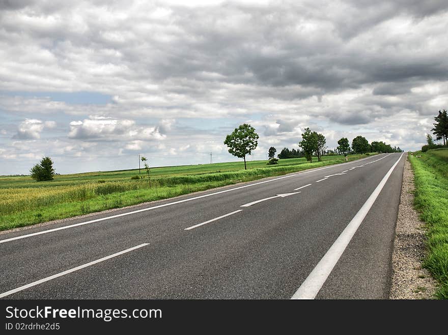 A deserted country road running through some green fields