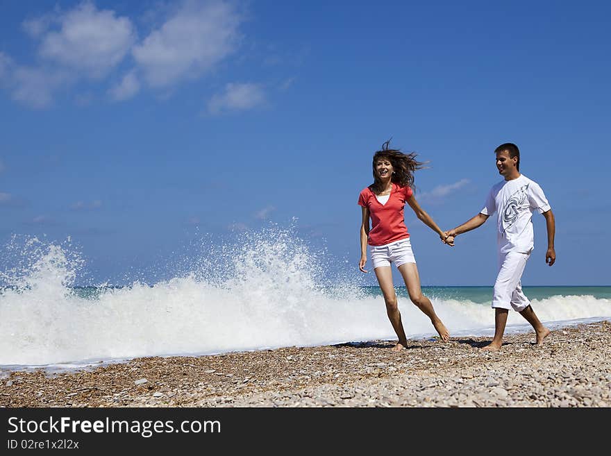 Young attractive couple holding hands while walking on the beach