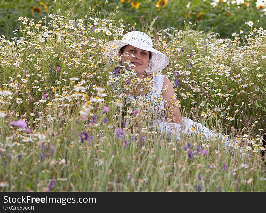 Lady in white dress and hat on a field with camomiles. Lady in white dress and hat on a field with camomiles