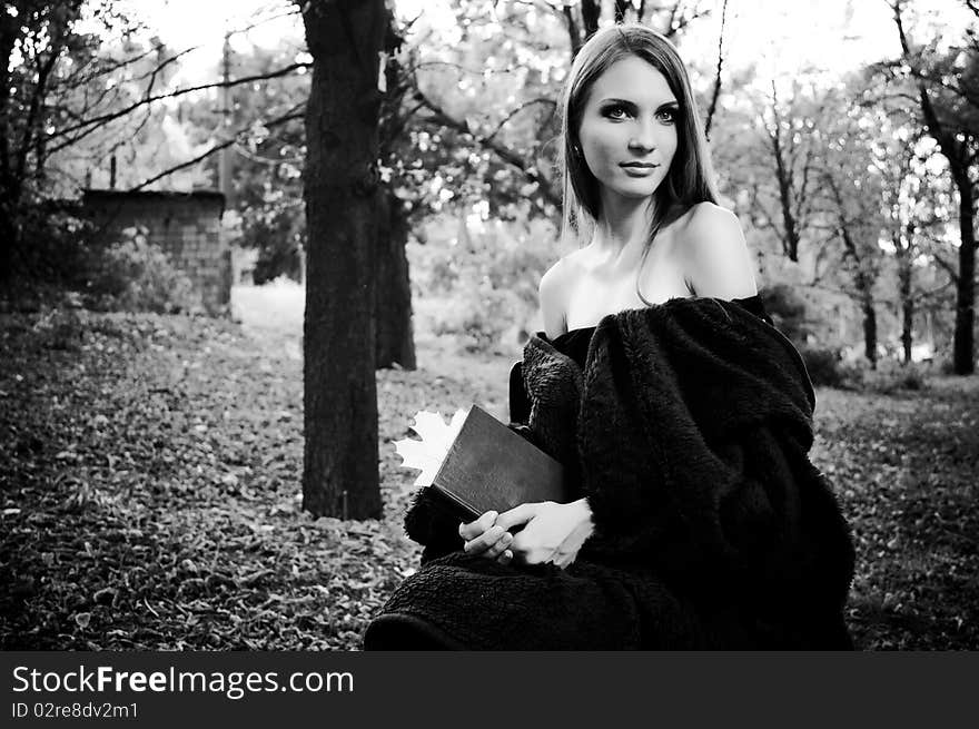 Beautiful woman sitting in forest, reading book, covered with plaid in black and white. Beautiful woman sitting in forest, reading book, covered with plaid in black and white