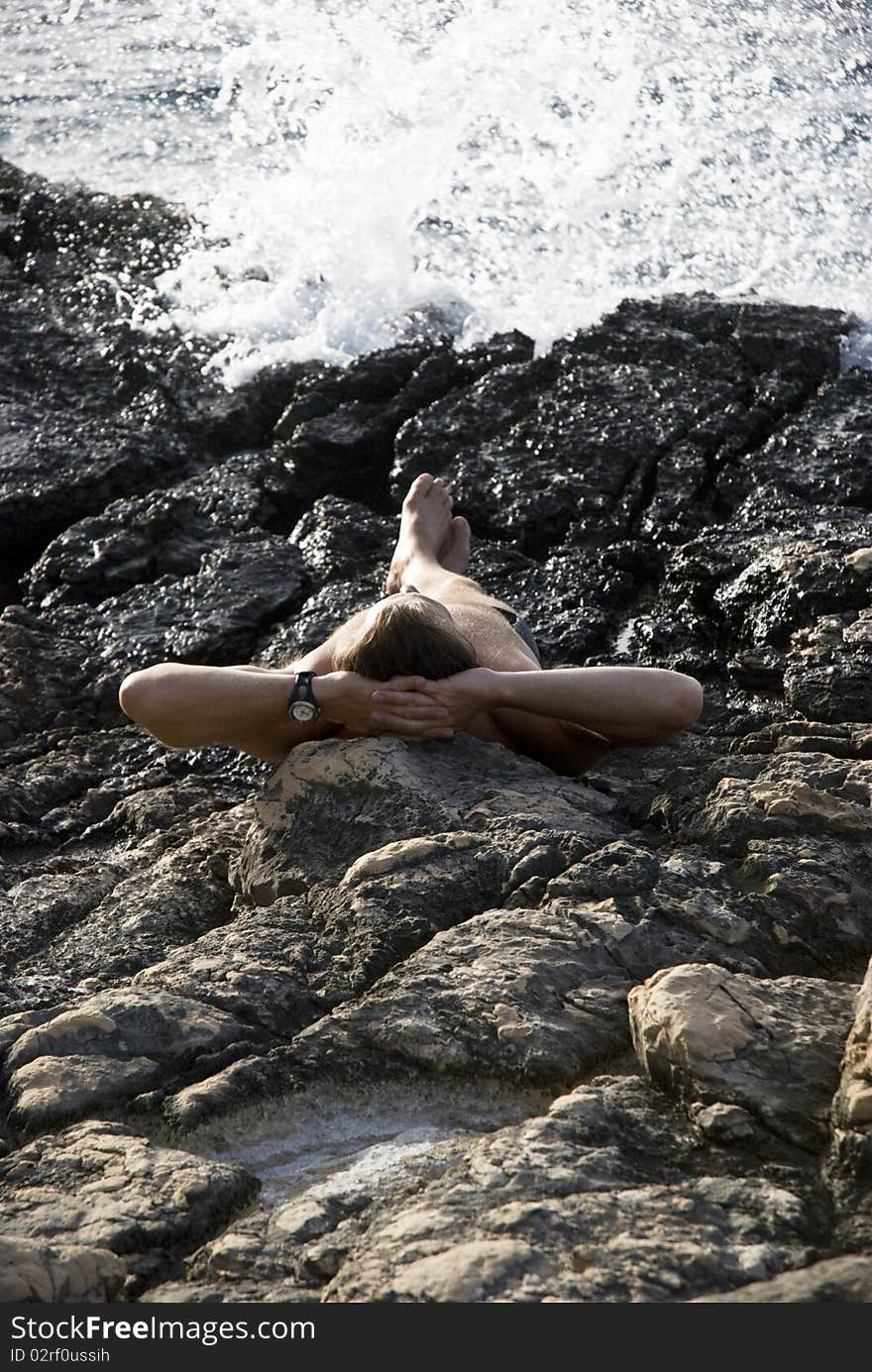 A color portrait photo of a caucasian man laying down on rocks and sunbathing next to the sea. A color portrait photo of a caucasian man laying down on rocks and sunbathing next to the sea.