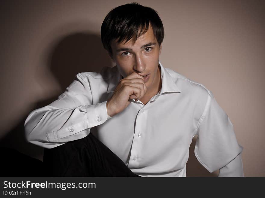 A man sits on a background of dark walls, a portrait lit one light source. A man sits on a background of dark walls, a portrait lit one light source