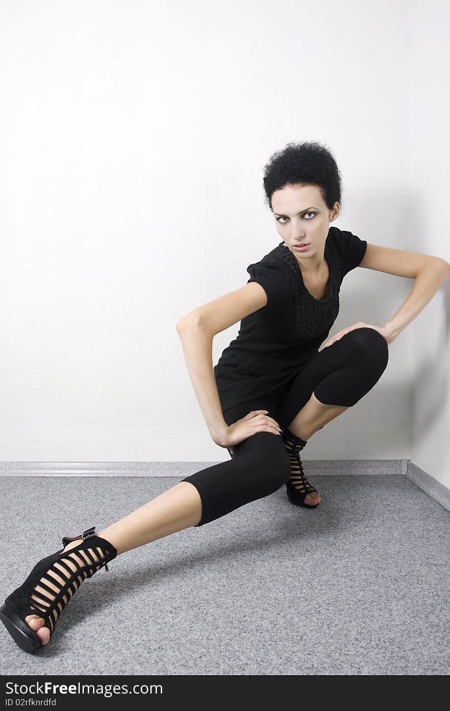 Beautiful fashion model in black dress and high heels sitting on the floor