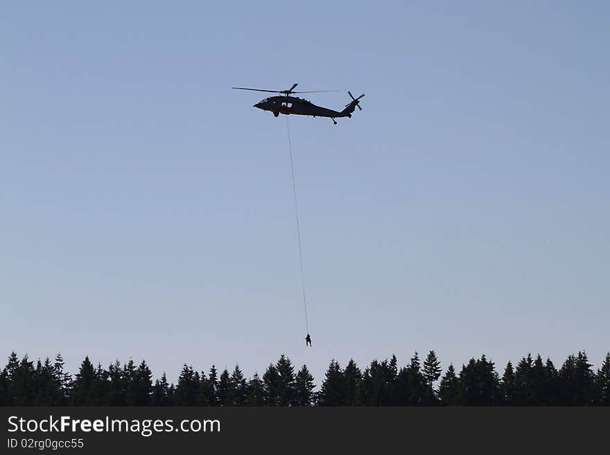 A helicopter hoists a person on a line from the forest. A helicopter hoists a person on a line from the forest.