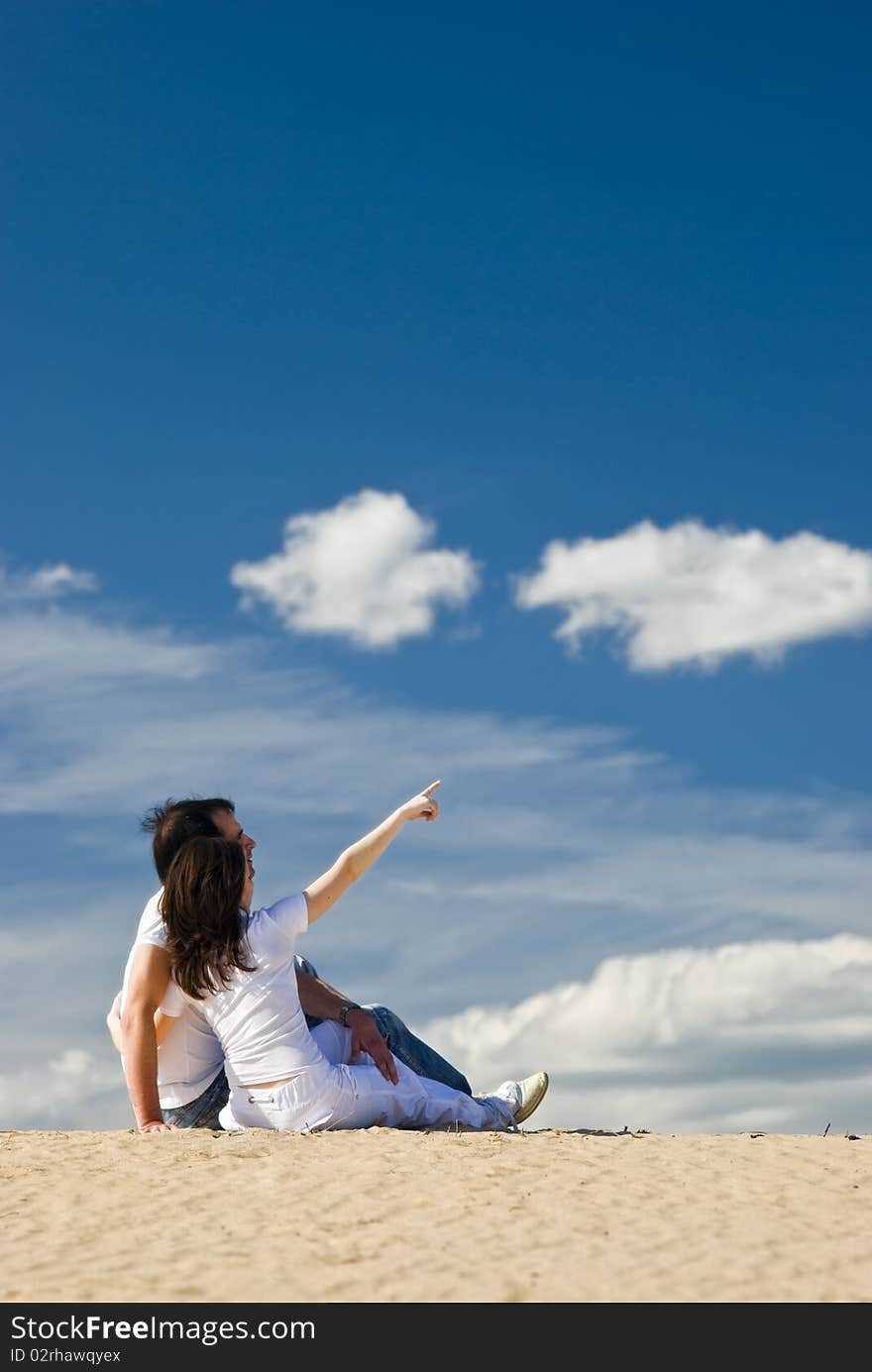 Young smiling couple sits on the dunes and man pointing at distance