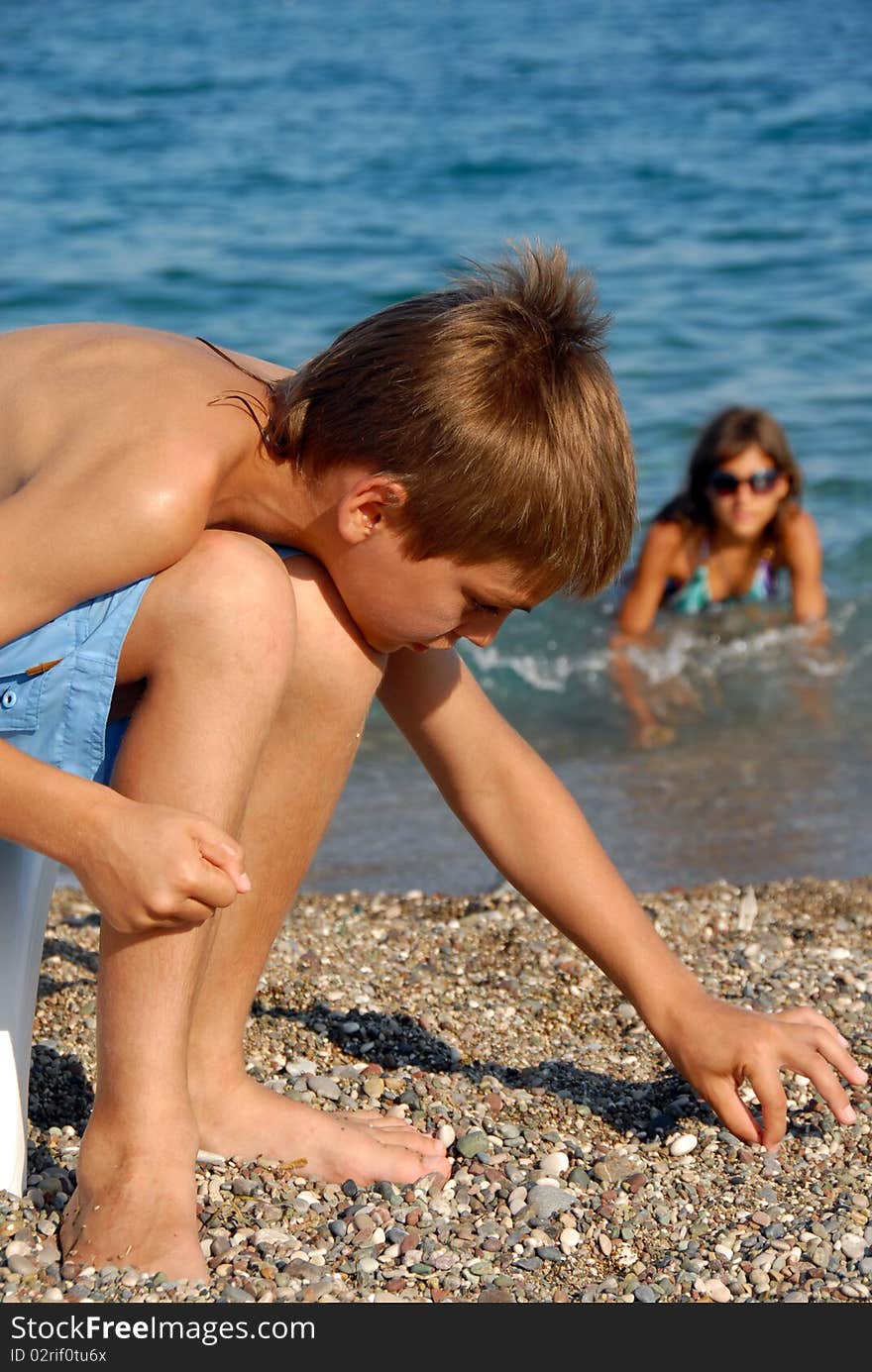 Little boy playing with rocks on pebble beach by blue sea. Little boy playing with rocks on pebble beach by blue sea