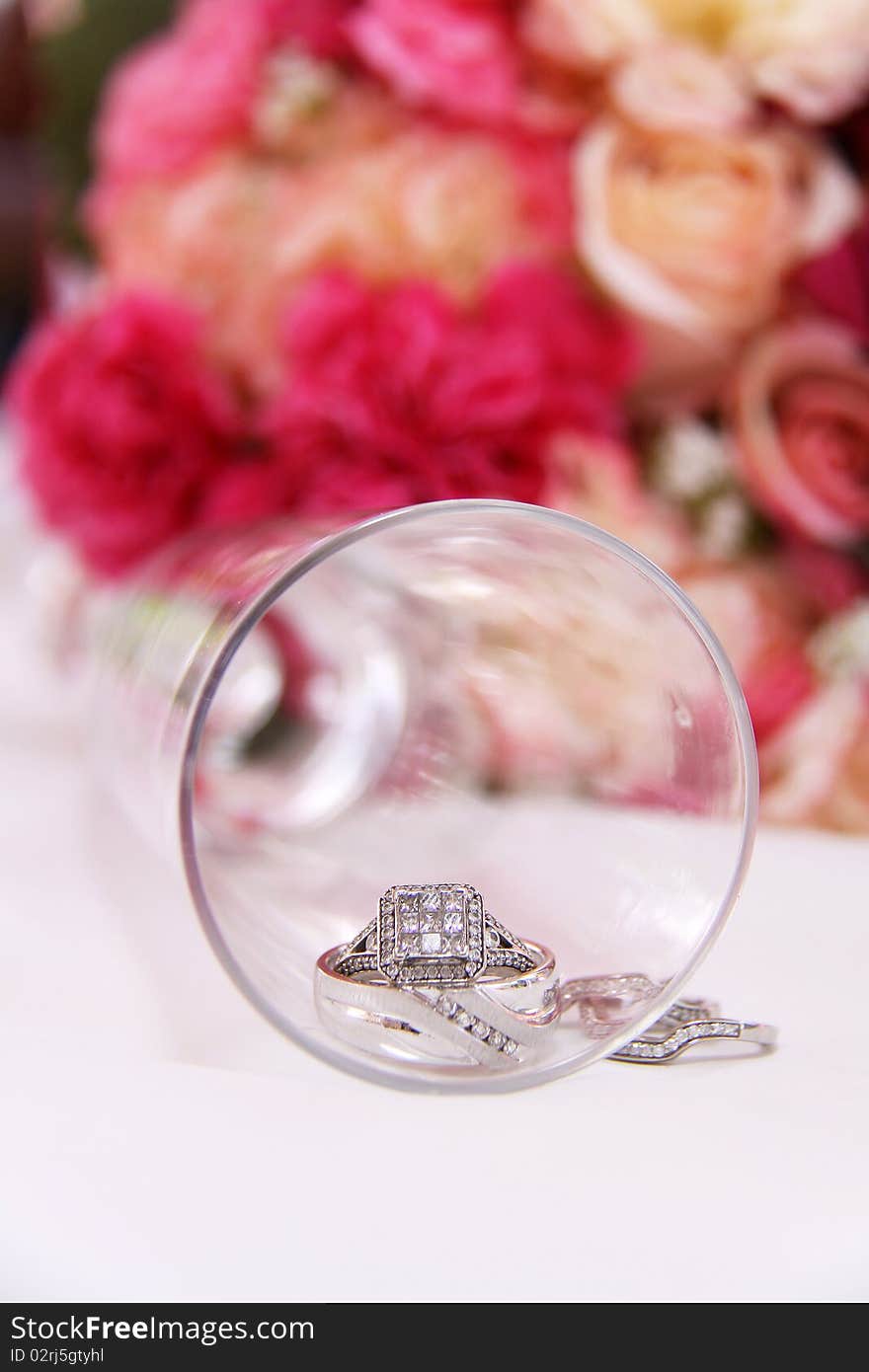 Wedding bands inside of a champagne glass. Colored roses in the background. Wedding bands inside of a champagne glass. Colored roses in the background.