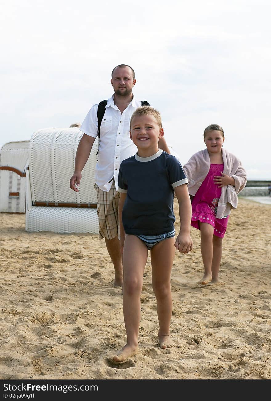 Young boy goes to her beach chair, in the back her sister and father follow him. Young boy goes to her beach chair, in the back her sister and father follow him