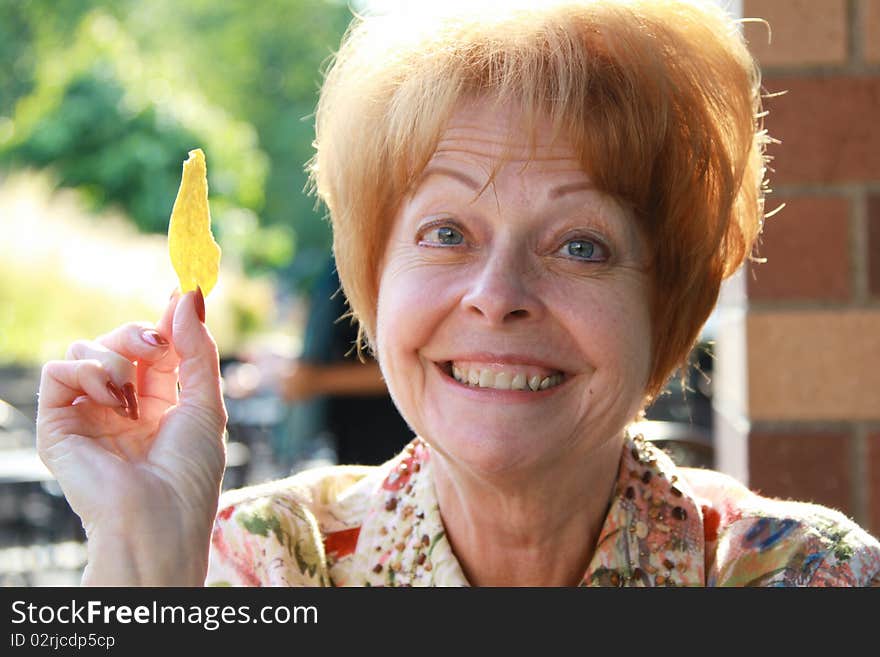 A mature woman smiles at dinner while holding a tortilla chip. A mature woman smiles at dinner while holding a tortilla chip