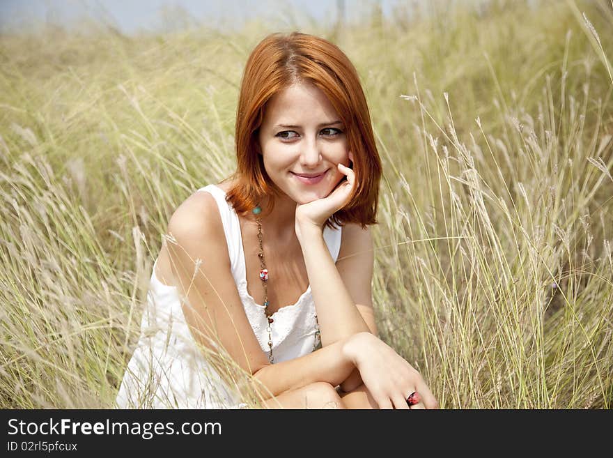 Beautiful red-haired girl at grass. Outdoor photo.