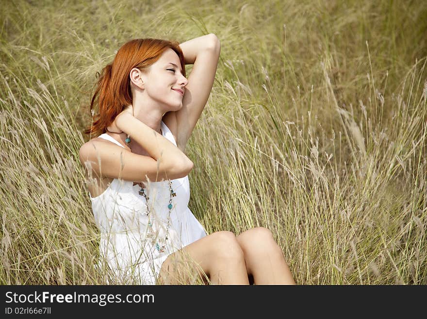 Beautiful red-haired girl at grass. Outdoor photo.