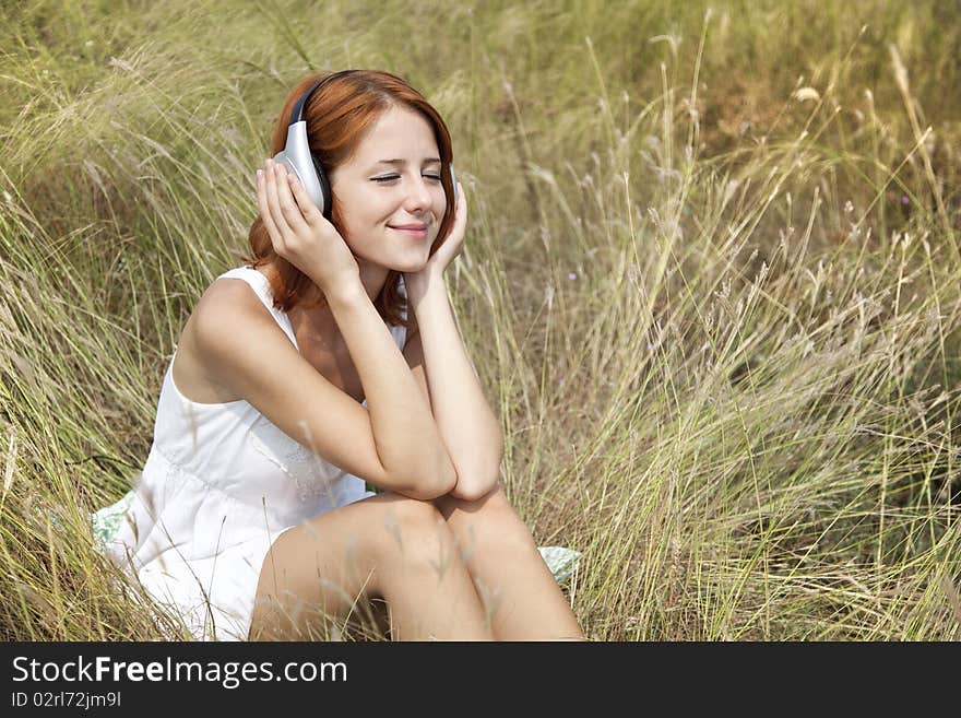 Beautiful red-haired girl at grass with headphones. Outdoor photo.