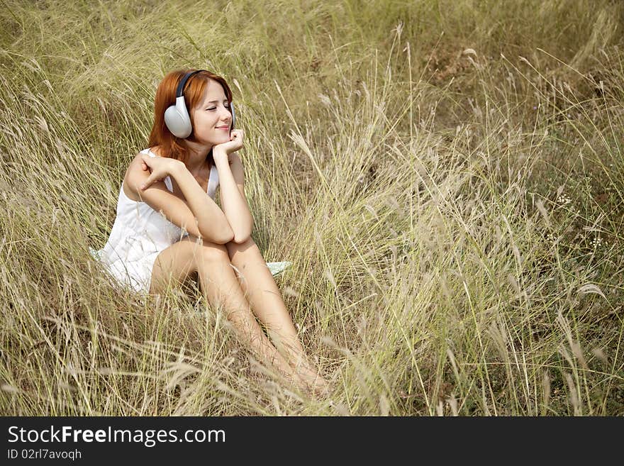 Beautiful red-haired girl at grass with headphones. Outdoor photo.