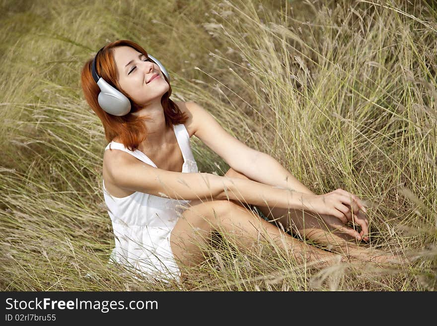 Beautiful red-haired girl at grass with headphones. Outdoor photo.