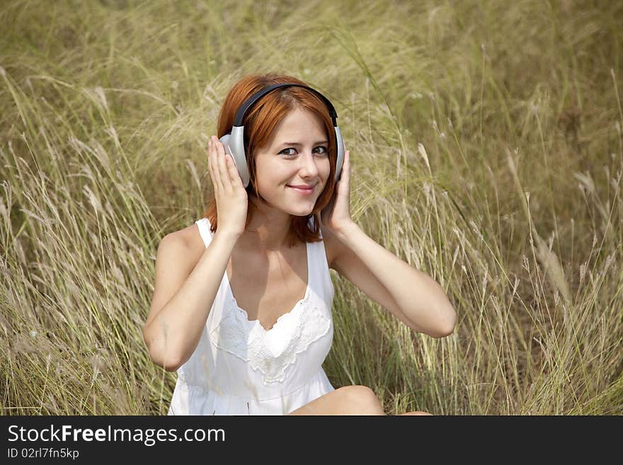 Beautiful red-haired girl at grass with headphones. Outdoor photo.