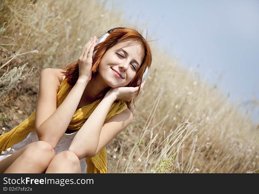 Beautiful red-haired girl at grass with headphones. Outdoor photo.