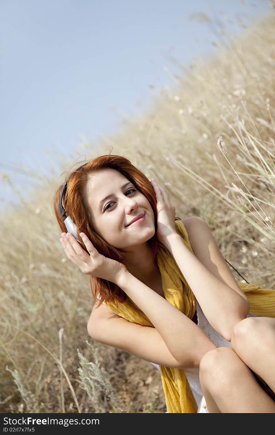 Beautiful red-haired girl at grass with headphones. Outdoor photo.