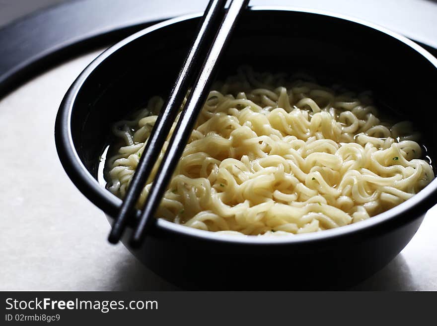 Asian noodle with chopstick served in a black bowl.