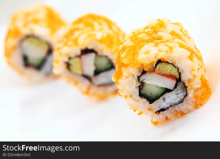 Japanese sushi covered in orange shrimp roe, arranged in single file and served on a white platter.