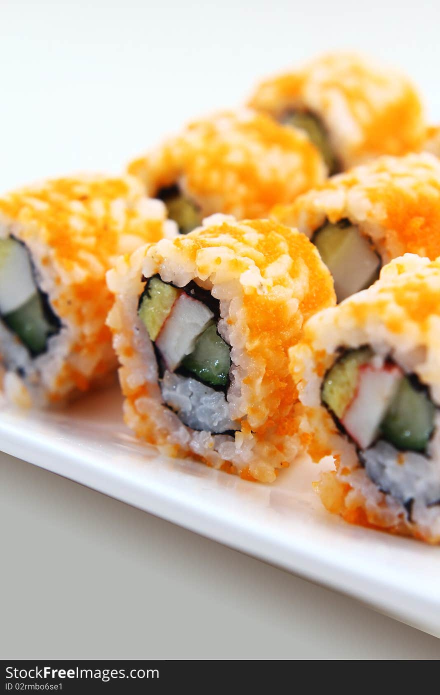 Japanese sushi covered in orange shrimp roe, arranged in single file and served on a white platter.