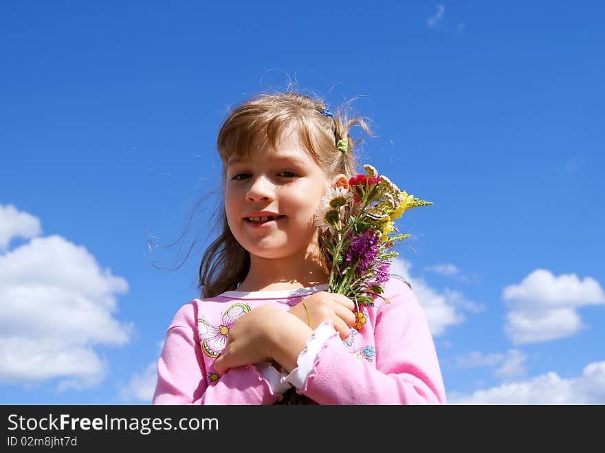 The beautiful girl stands against the sky with a bouquet of wild flowers. The beautiful girl stands against the sky with a bouquet of wild flowers