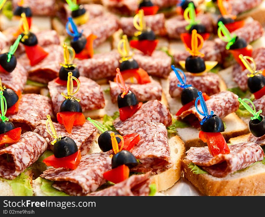 Many small sandwiches with salami and olives on skewers. Many small sandwiches with salami and olives on skewers.