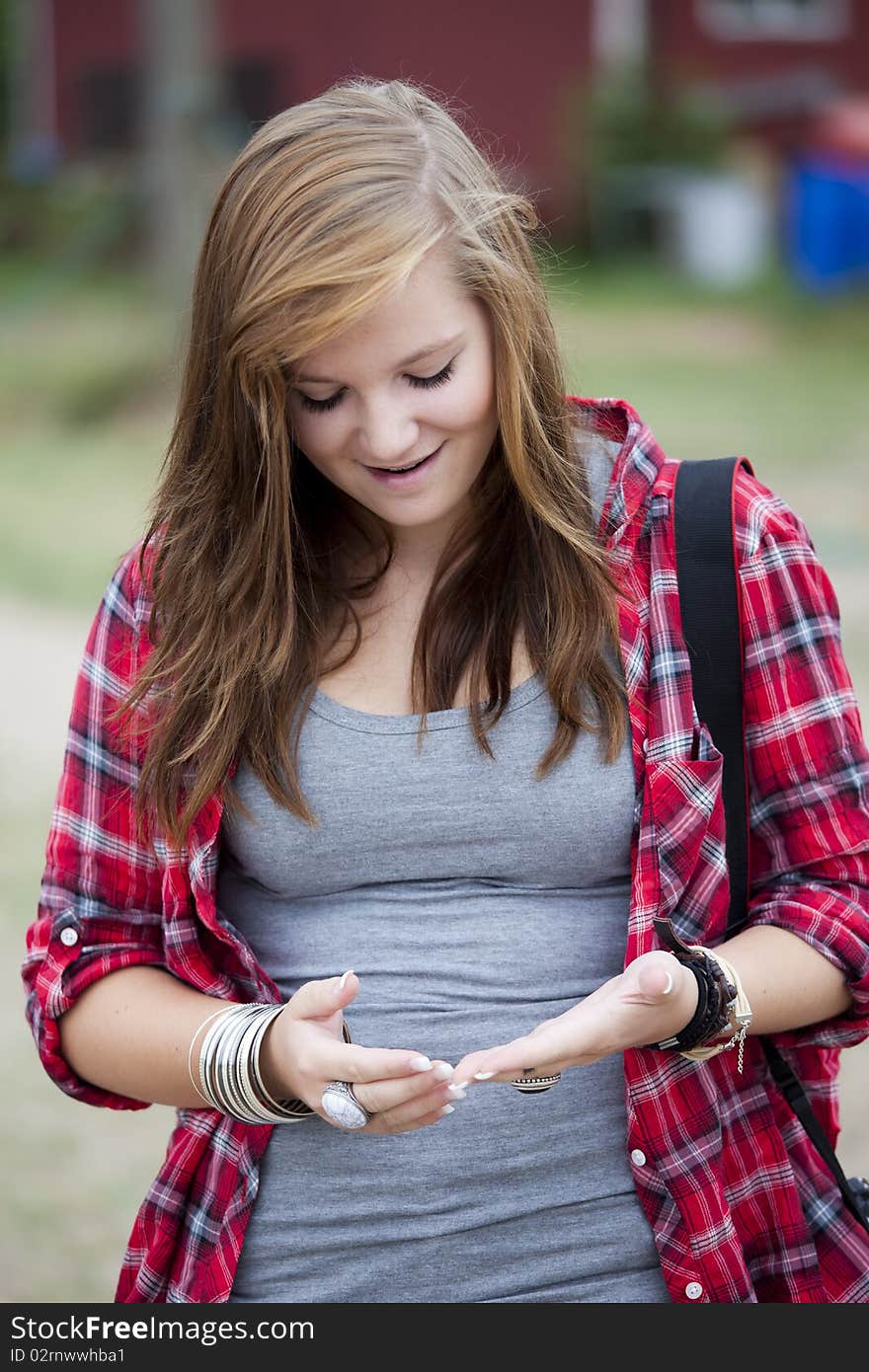 Teenage girl standing up smiling and looking at her hands. Teenage girl standing up smiling and looking at her hands.