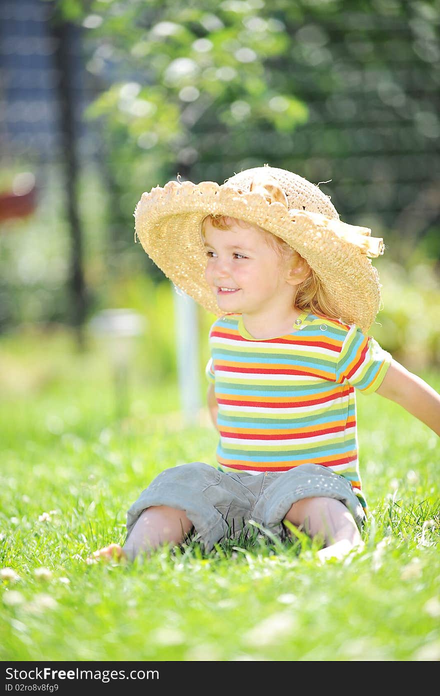 Little girl in straw hat sitting on green grass