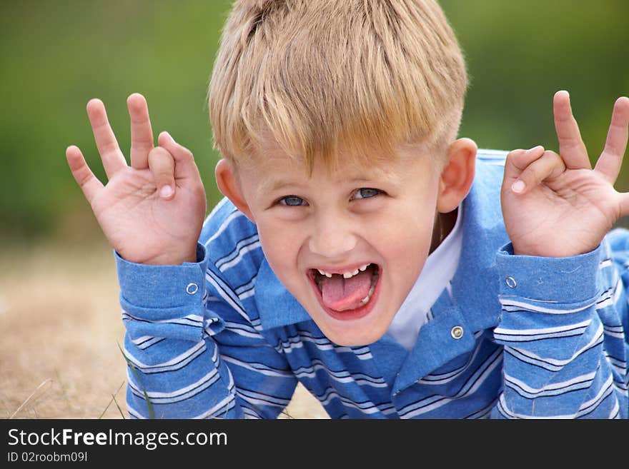 Boy builds a merry faces against the backdrop of green meadows. Boy builds a merry faces against the backdrop of green meadows