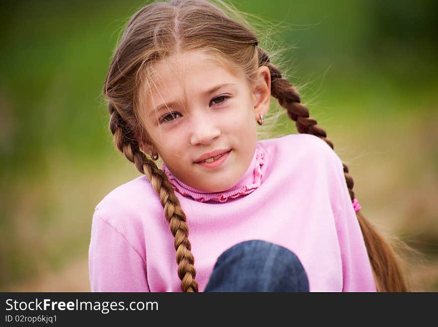 Portrait of little girl with pigtails smiling at the camera against  background of green