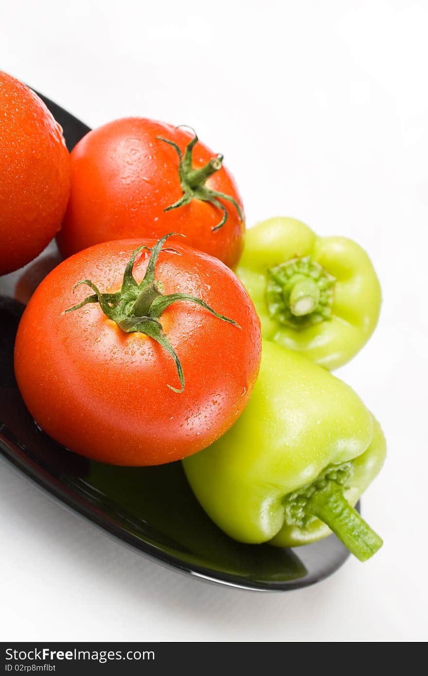 Fresh tomatoes and peppers washed and placed in a black ceramic plate isolated on white background