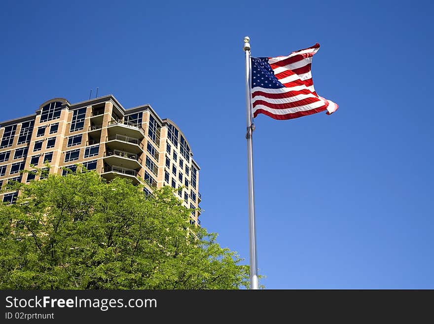 A US flag waves in the wind by a building partly behind a tree. A US flag waves in the wind by a building partly behind a tree.