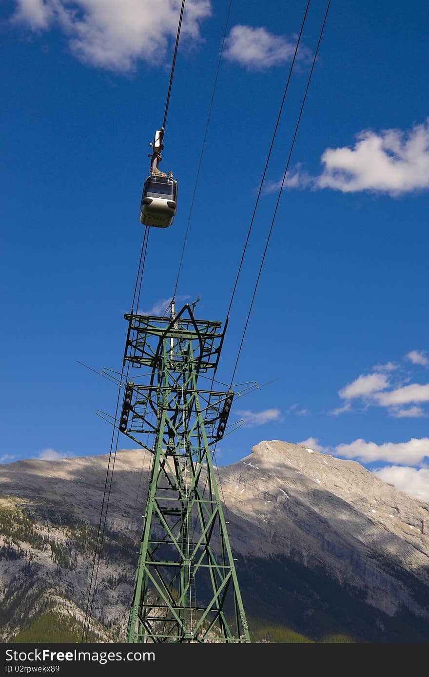 Banff Sulphur Mountain Gondola on a blue sky with snow peaked Rocky Mountains in background.