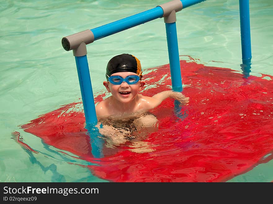 Young boy with cap and swim goggles on red platform in indoor pool. Young boy with cap and swim goggles on red platform in indoor pool