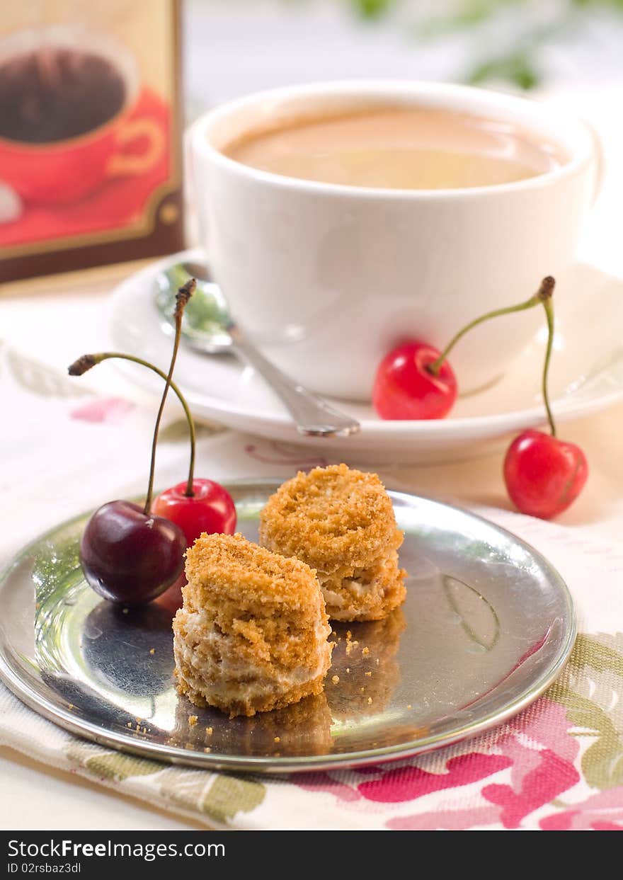 Two small honey cakes on a plate with cherry and coffee in background. Two small honey cakes on a plate with cherry and coffee in background.